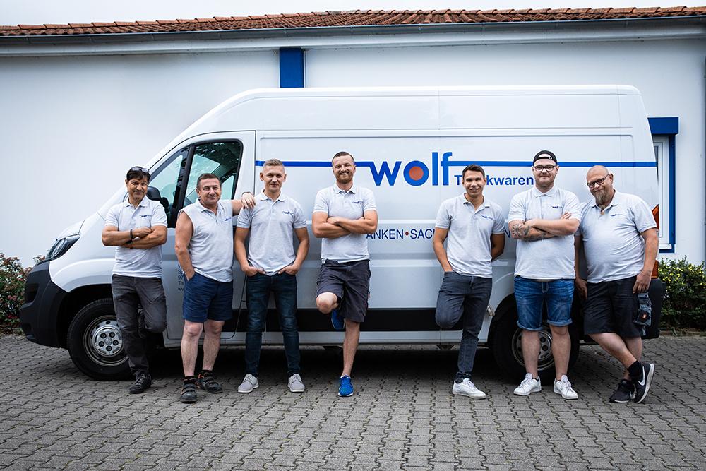 Techniker Sieben Männer mit grauem Poloshirt, die an einen weißen Transporter der Firma Wolf gelehnt sind.