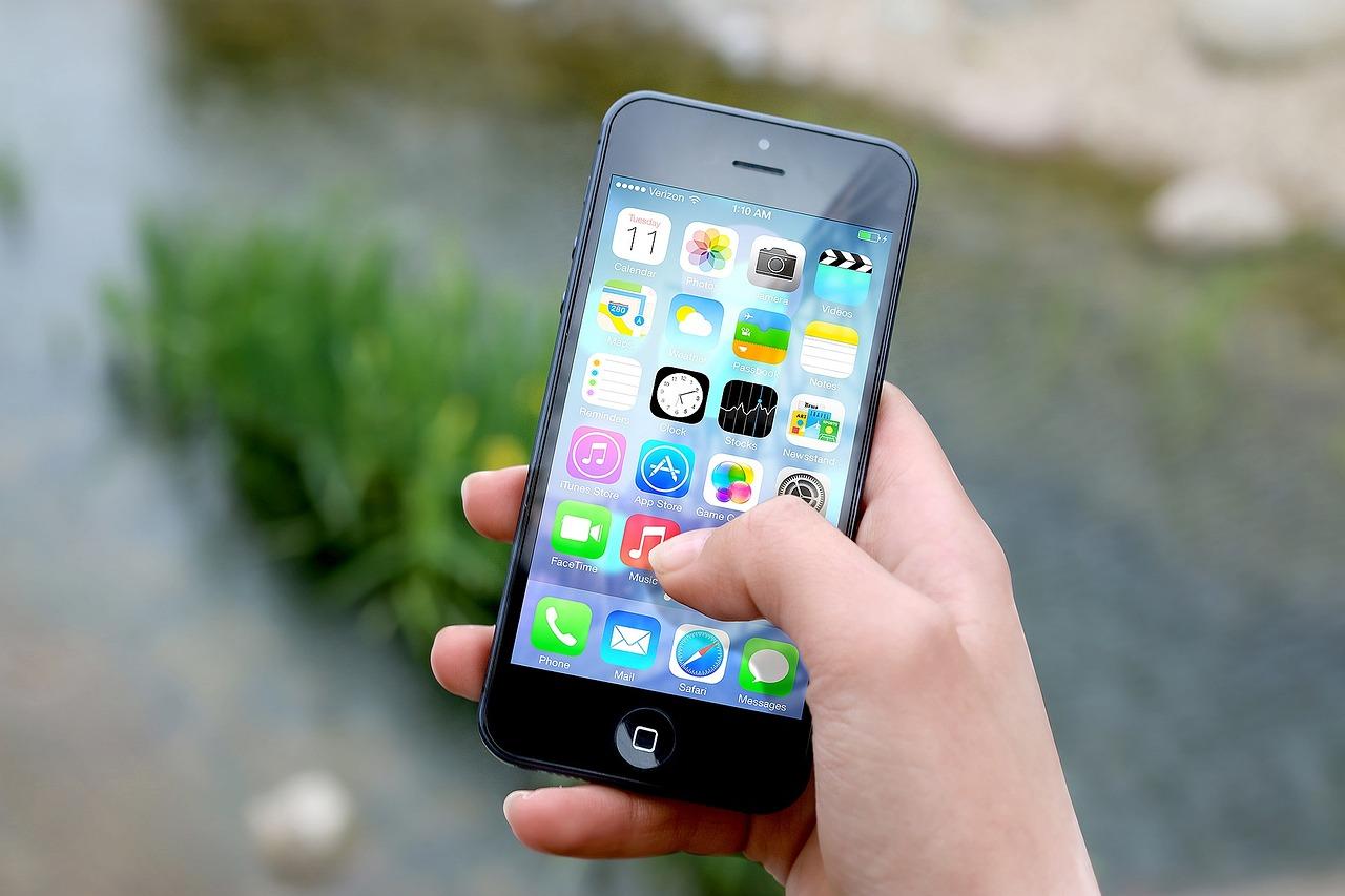 Eine Hand streckt ein iPhone nach oben, auf dem das Menü geöffnet ist.