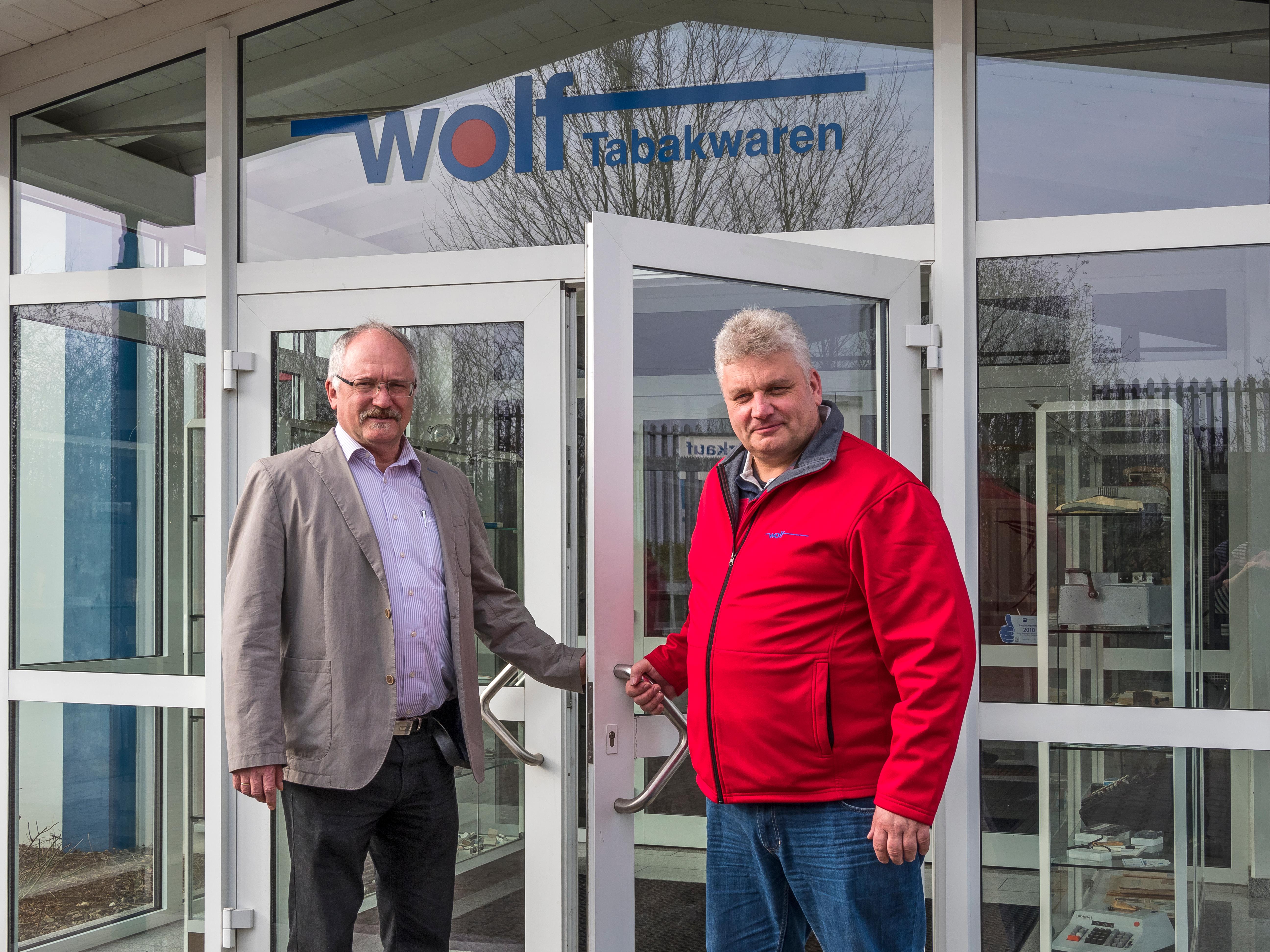 Zwei ältere Männer, die gemeinsam die Eingangstür der Firma Wolf öffnen.