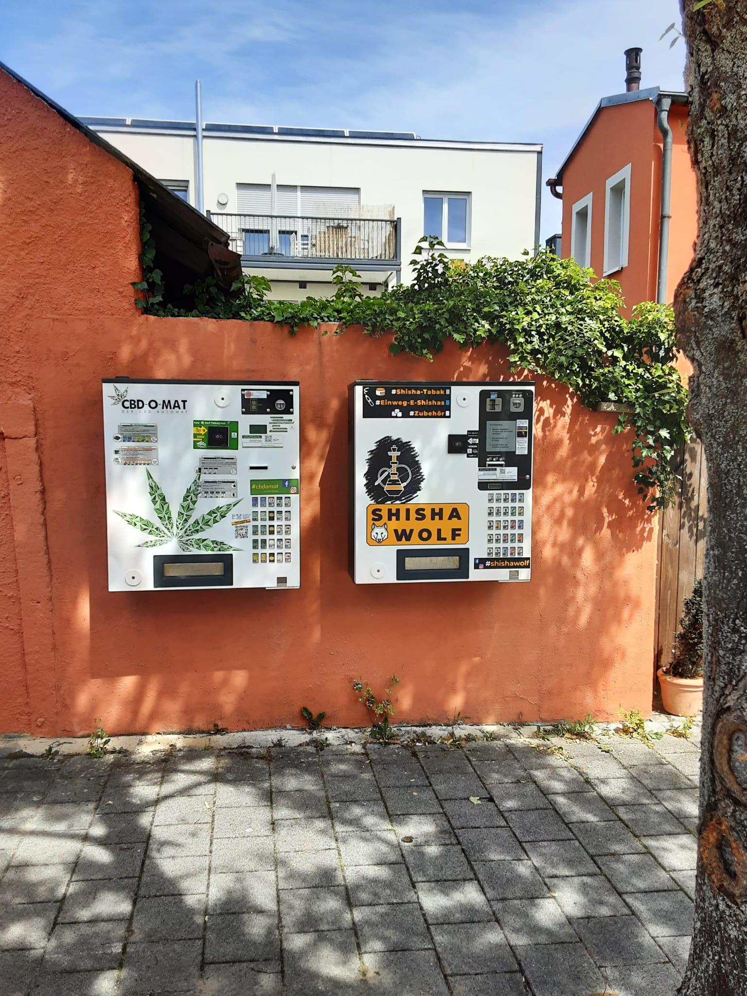 Foto von einem CBD-Automaten und einem Shisha-Automaten an einer orangenen Hauswand