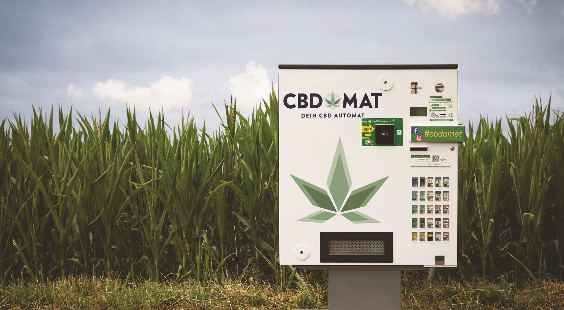 Ein CBD-Automat auf einem Ständer vor einem grünen Maisfeld