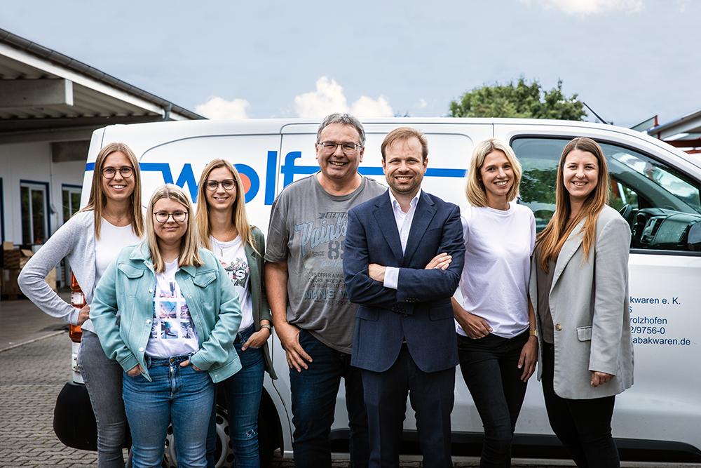 Sieben Mitarbeiter der Firma Wolf in Alltagskleidung stehen vor einem weißen Transporter und lächeln in die Kamera.