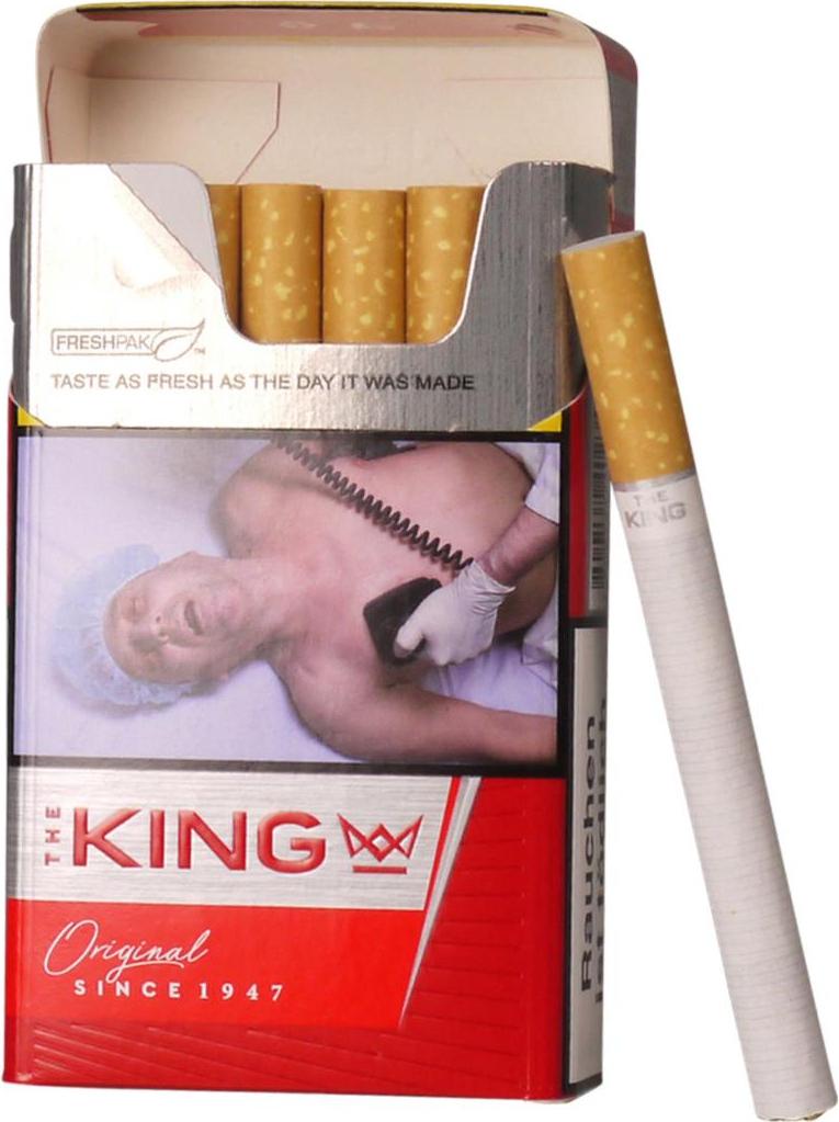 Geöffnete rote und weiße Zigarettenpackung King Red mit 20 Stück, zeigt eine silberne Folie mit dem Motiv eines Mannes, der auf einem Bett liegt und mit einem Telefon verbunden ist. Neben der Packung liegt eine einzelne weiße Zigarette.