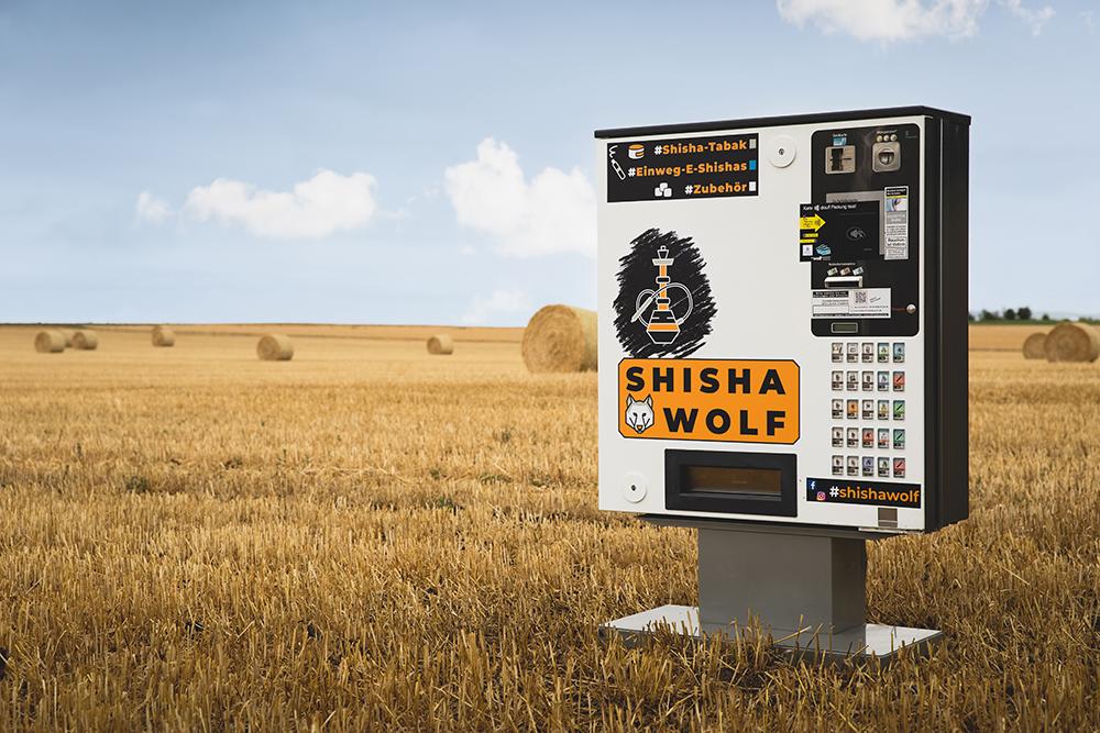 Shisha Automat Ein Shisha-Automat, der gelb-schwarz beklebt ist und auf einem abgeernteten Getreidefeld steht.