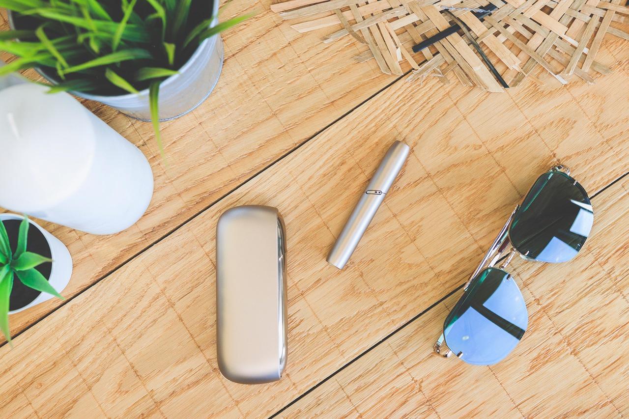 IQOS auf Tisch Die Sicht auf einen Schreibtisch, auf dem eine Sonnenbrille und ein IQOS Tabakerhitzer liegt.