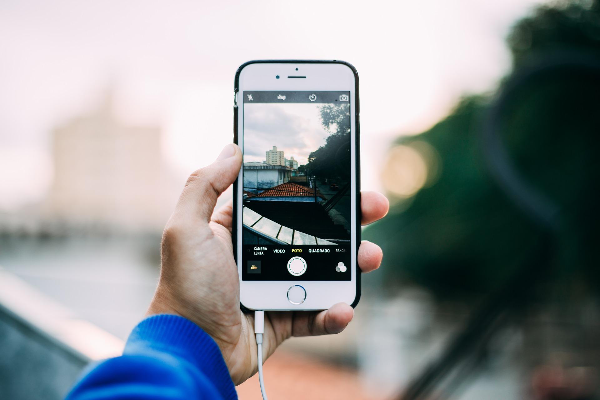 Eine Hand streckt ein iPhone in die Kamera und macht ein Foto von einer städtischen Umgebung.