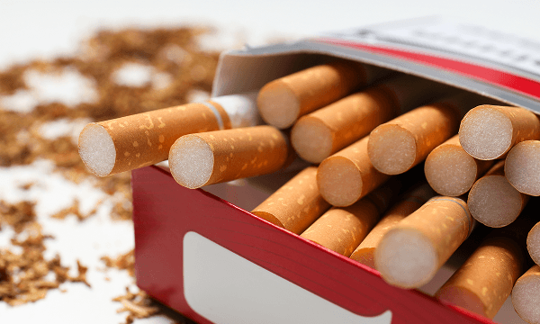 Eine offene Schachtel Zigaretten liegen auf einer weißen Oberfläche, im Hintergrund loser Tabak.