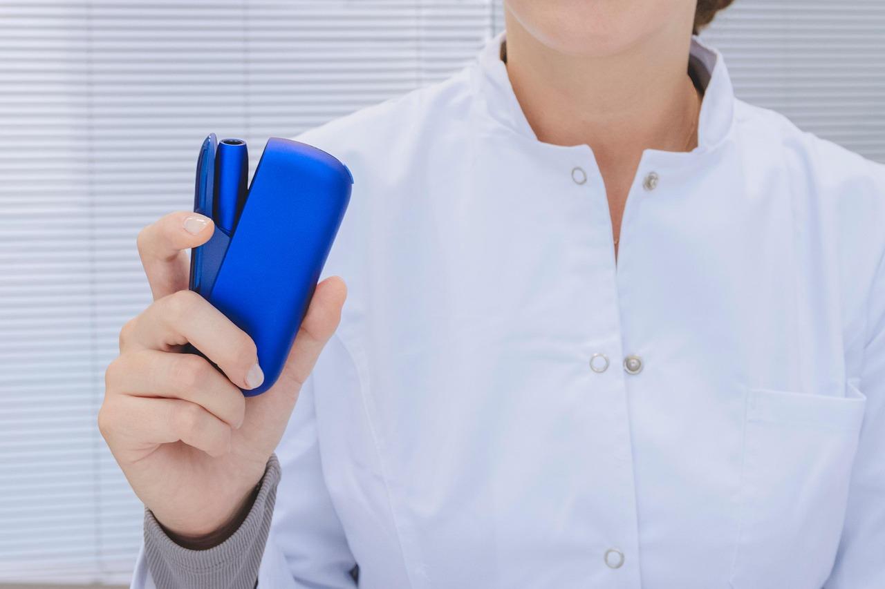 IQOS blau Ein Mensch in weißem Kittel hält einen blauen IQOS Tabakerhitzer in der Hand.