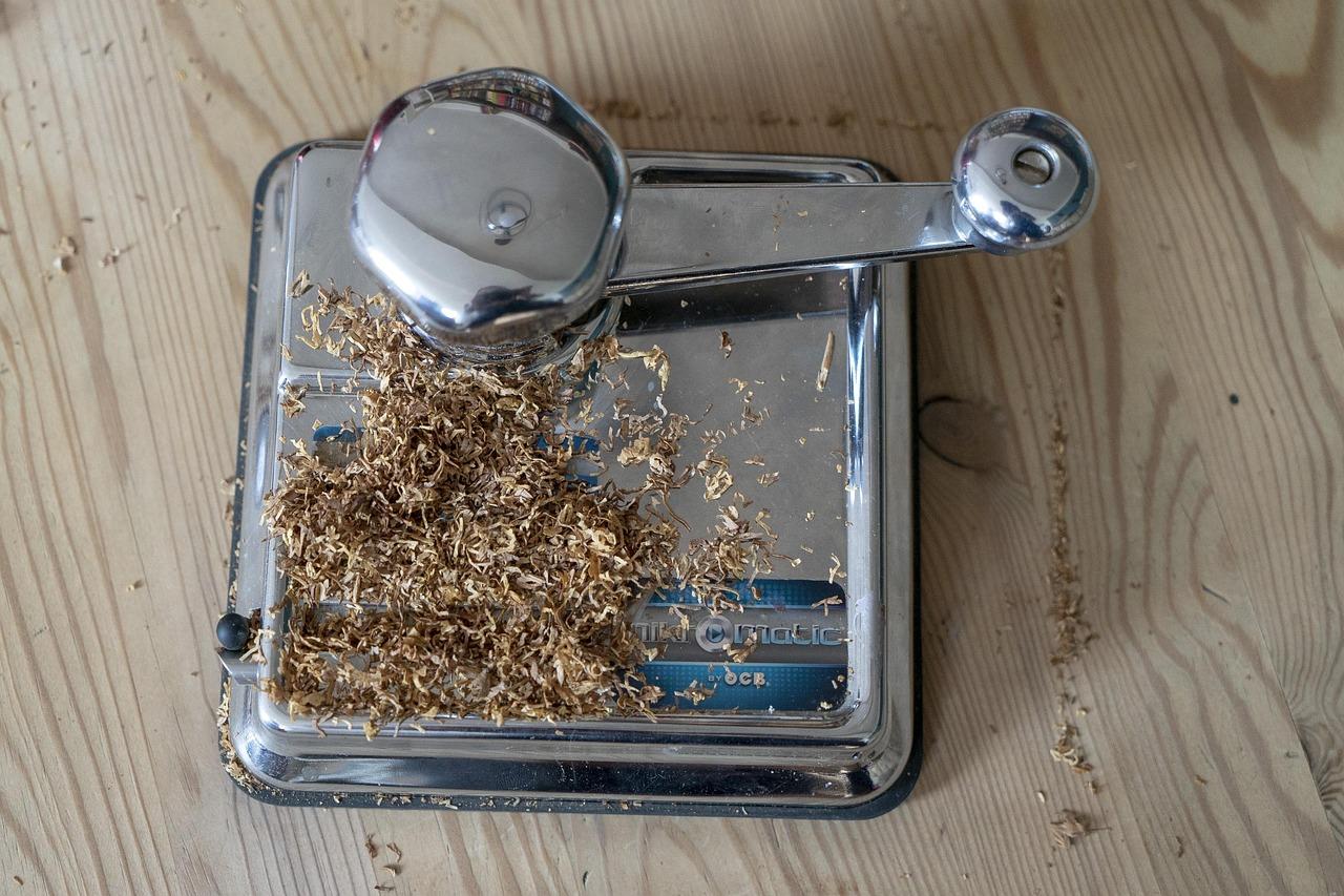 Eine silberne Zigaretten-Stopfmaschine mit losem Tabak auf einem Tisch.